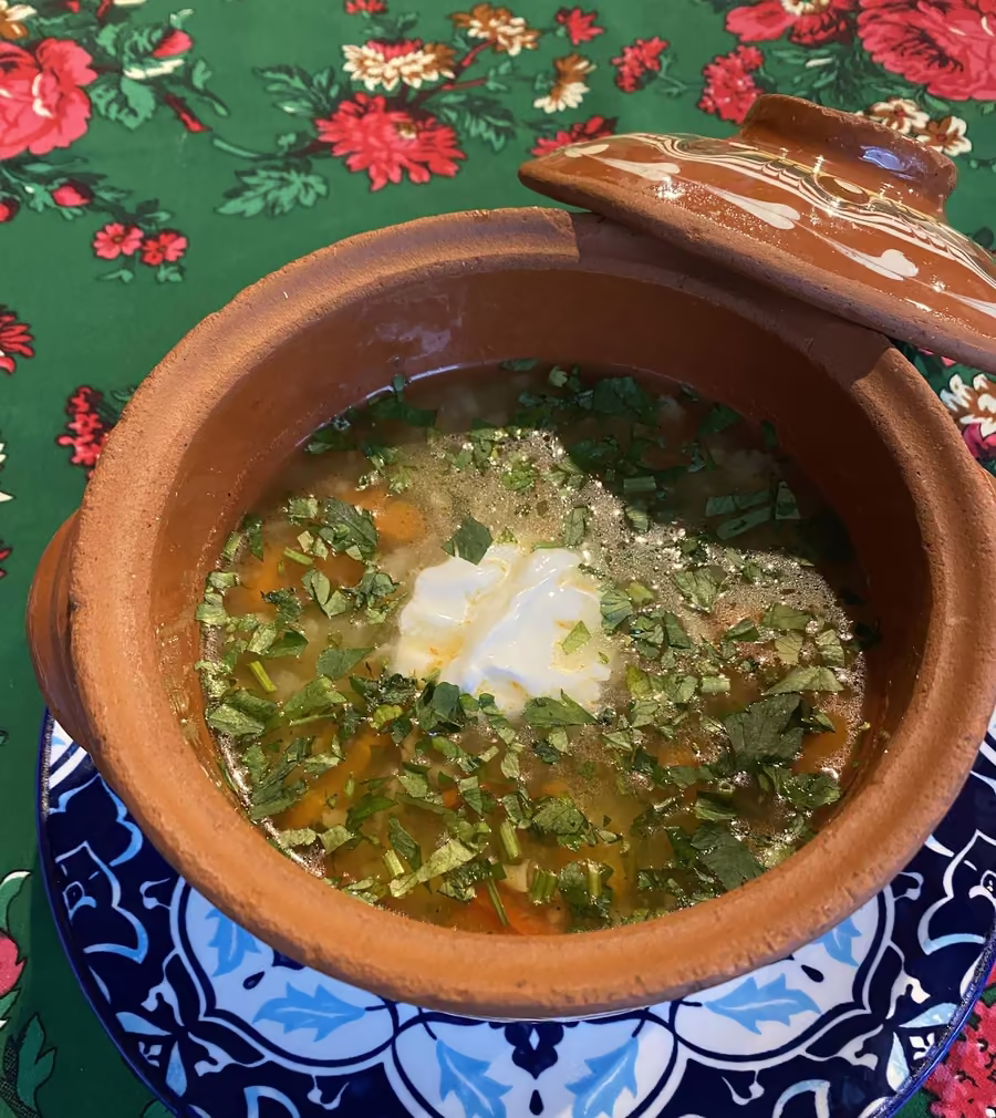 Zupa w glinianym garnku na talerzu we wzory, na obrusie w róże